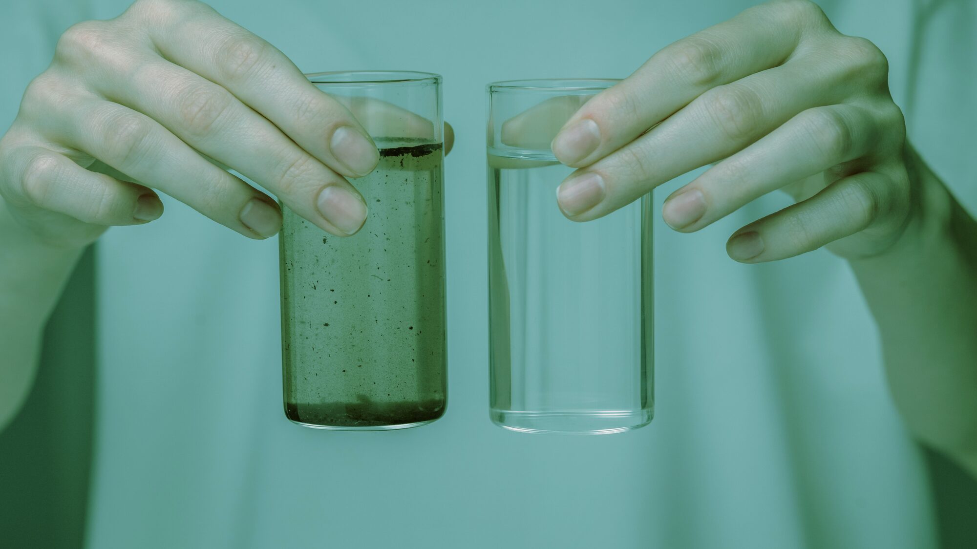 Gloved hands holding two beakers of water samples ready for testing