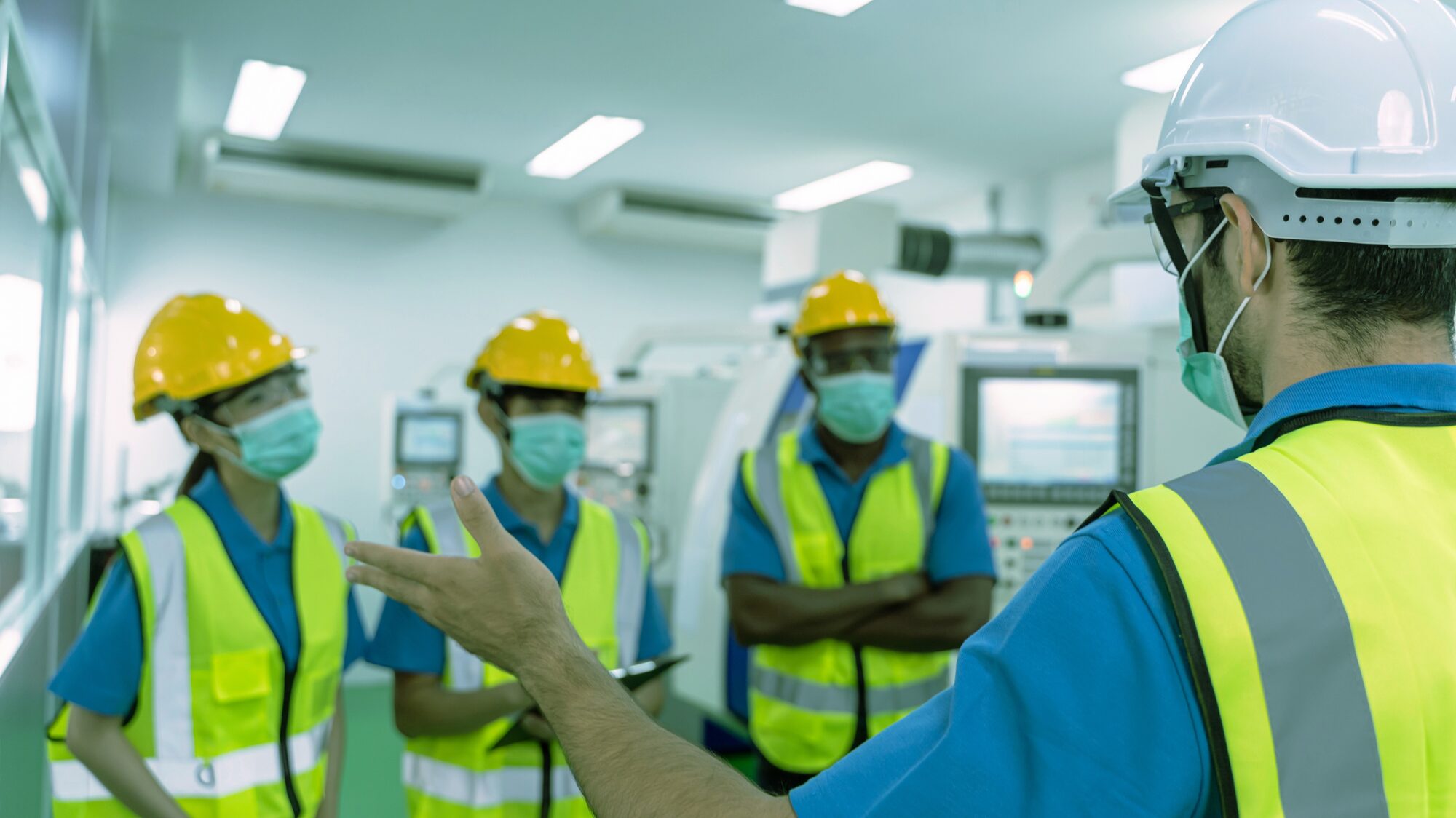Plant operators in hard hats being briefed at a control panel